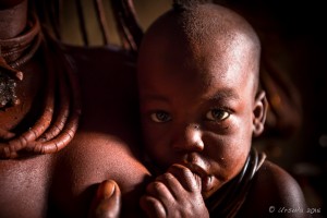 Himba baby nursing in a dark hut, Otjomazeva Village Namibia