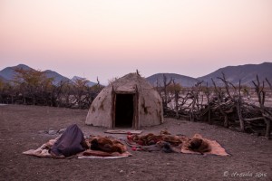 People in bed rolls in front of Himba huts, Otjomazeva Village Namibia