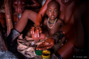 Himba woman with a child mixing ochre paste, Otjomazeva Village Namibia