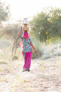 Woman in pink veil walking with water canisters , Khiyasariya village, India