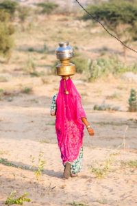 Woman in pink veil walking with water canisters , Khiyasariya village, India
