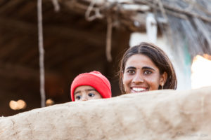 A smiling woman looking over a clay wall, Khiyasariya village, India