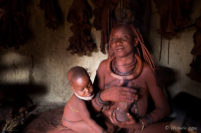 Himba woman with smoking pot and an infant on her knee, Otjomazeva Village, Kunene Namibia 