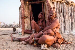 Two old Himba women seated with a sleeping child, Otjomazeva Village, Kunene Namibia