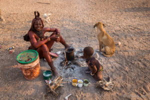 Young Himba woman making Breakfast, with a baby and a dog, Otjomazeva Village, Kunene Namibia