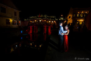 Vietnamese couple posing under lights at the floodlit Japanese Bridge, after dark, Hoi An, Vietnam