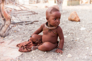 Portrait: Himba baby sitting on gravel, Kunene Region Namibia