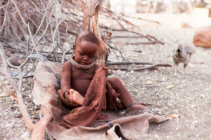 Portrait: Himba baby examining her foot, Kunene Region Namibia
