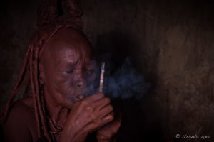 Old Himba woman smoking a pipe in a dark hut, Kunene, Namibia