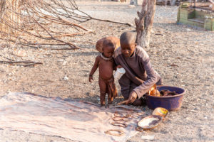 A Himba youth and baby Putting Trinkets out on a cowhide, Kunene Region, Namibia