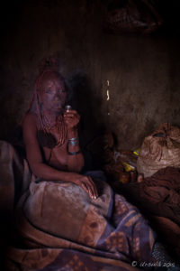 Old Himba woman smoking in a dark hut, Kunene Region, Namibia