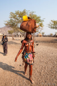 A young Himba woman carrying a Loaded Bundle on her head, Kunene Region Namibia