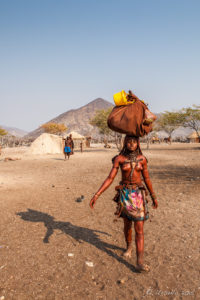 A young Himba woman carrying a Loaded Bundle on her head, Kunene Region Namibia