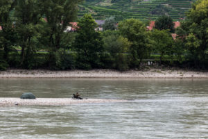 A man sitting on a chair on a sandy spit, fishing on the Danube, Wachau Valley Austria