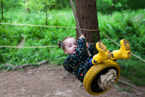 Toddler on a tire swing, The Weir riverside garden, Herefordshire, UK