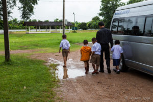 Thai man and boys in school uniform walking across a muddy road, Chumchon Lae Luang Prasit Wittaya Primary School speaking to young pupils, Chiang Mai Thailand