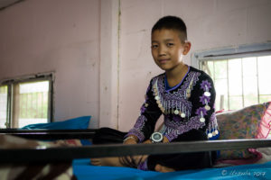 Hmong boy in traditional costume on a Dormitory bunkbed, Santisuk School, Chiang Mai Thailand