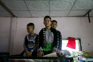Hmong boy in traditional costume on a Dormitory bunkbed, Santisuk School, Chiang Mai Thailand