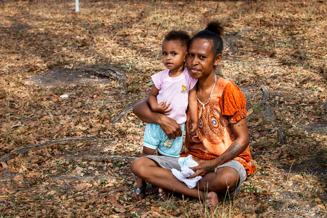 Papuan Mother seated in grass with her toddler, Port Moresby, Papua New Guinea 