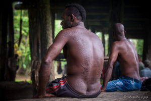 Two seated crocodile men with scarification running down their backs sitting in the Kanganaman spirit house, PNG