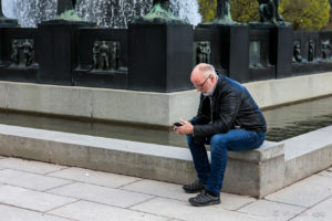 A man and his phone at the base of the fountain, Frogner Park Oslo Norway.