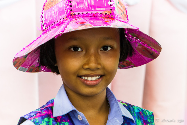 Portrait: smiling Thai Schoolgirl in a pink Recycle Hat, Bang Khun Thien Thailand.