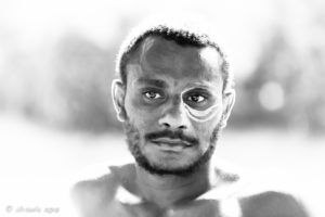 B&W portrait of a Papuan man being face-painted with cassowary eyes, Middle Sepik, PNG