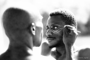 B&W portrait of a Papuan man being face-painted with cassowary eyes, Middle Sepik, PNG