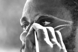 B&W portrait of a Papuan man being face-painted with cassowary eyes, Middle Sepik, PNG