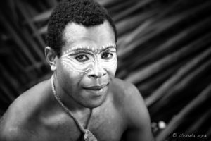 B&W portrait of a Papuan man being face-painted with cassowary eyes, Middle Sepik, PNG