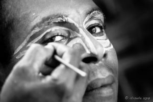 B&W portrait of a Papuan man being face-painted with cassowary eyes, Middle Sepik, PNG