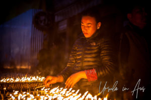 Tibetan Buddhist woman lighting candles at Boudhanath Stupa, Kathmandu.