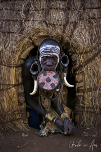 Mursi woman in a lip plate in the doorway of a hut, Omo Valley Ethiopia