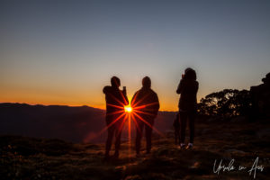 Sunburst through three people silhouetted at sunrise, Thredbo, NSW Australia