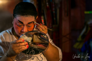 Chinese opera performer applying eyebrow pencil in a mirror, Chao Zhou Shi Kong Shrine, Bangkok