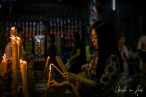 Woman lighting devotional candles, Chao Zhou Shi Kong Shrine, Bangkok