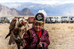 Small Kazakh child in traditional eagle-hunter dress and a hooded falcon, Golden Eagle Festival, Olgii Mongolia
