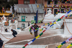 Man guiding strings of prayer flags down Boudhanath stupa, Kathmandu Nepal