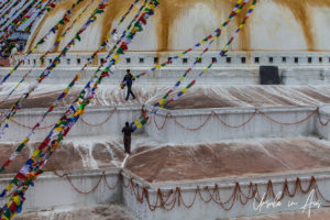 Men guiding strings of prayer flags down Boudhanath stupa, Kathmandu Nepal