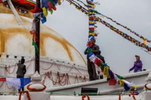 Man guiding strings of prayer flags down Boudhanath stupa, Kathmandu Nepal