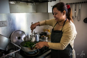 A Nepali woman in a kitchen stirring greens.