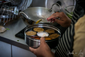 Woman's hands seaoning a pot on a stove using a spice tin.