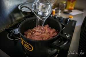 Pouring water over chicken in a pot on a stove.