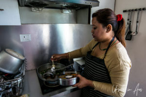 Woman's hands seaoning a pot on a stove using a spice tin.