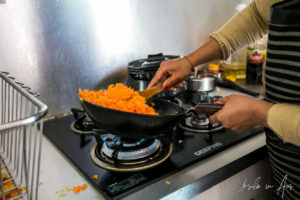 Hands stirring grated carrot in a wok.