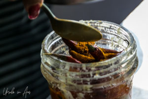 Adding a spoon of spice in ghee to a blender of chillies.