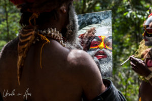 Western Highland man applying face paint in a hand mirror, Paiya Village, Papua New Guinea.