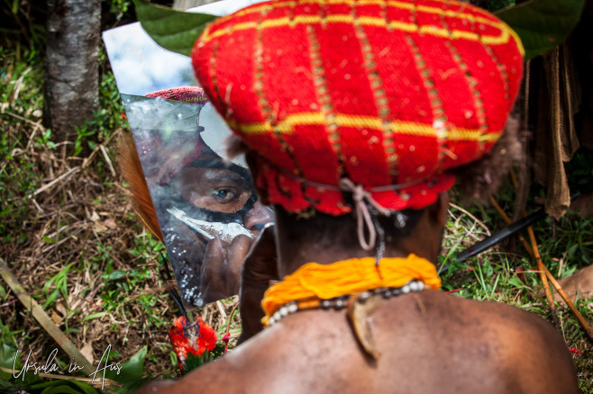 Back view: Western Highlands man applying face-paint, Paiya Village, Papua New Guinea.