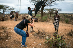 Photographer, a male subject and a man holding a softbox, in a Hamar village, Omo Valley Ethiopia.