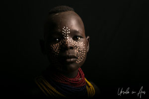 Portrait against black: painted Kara girl in red and yellow beads, Dus Village, Omo Valley Ethiopia